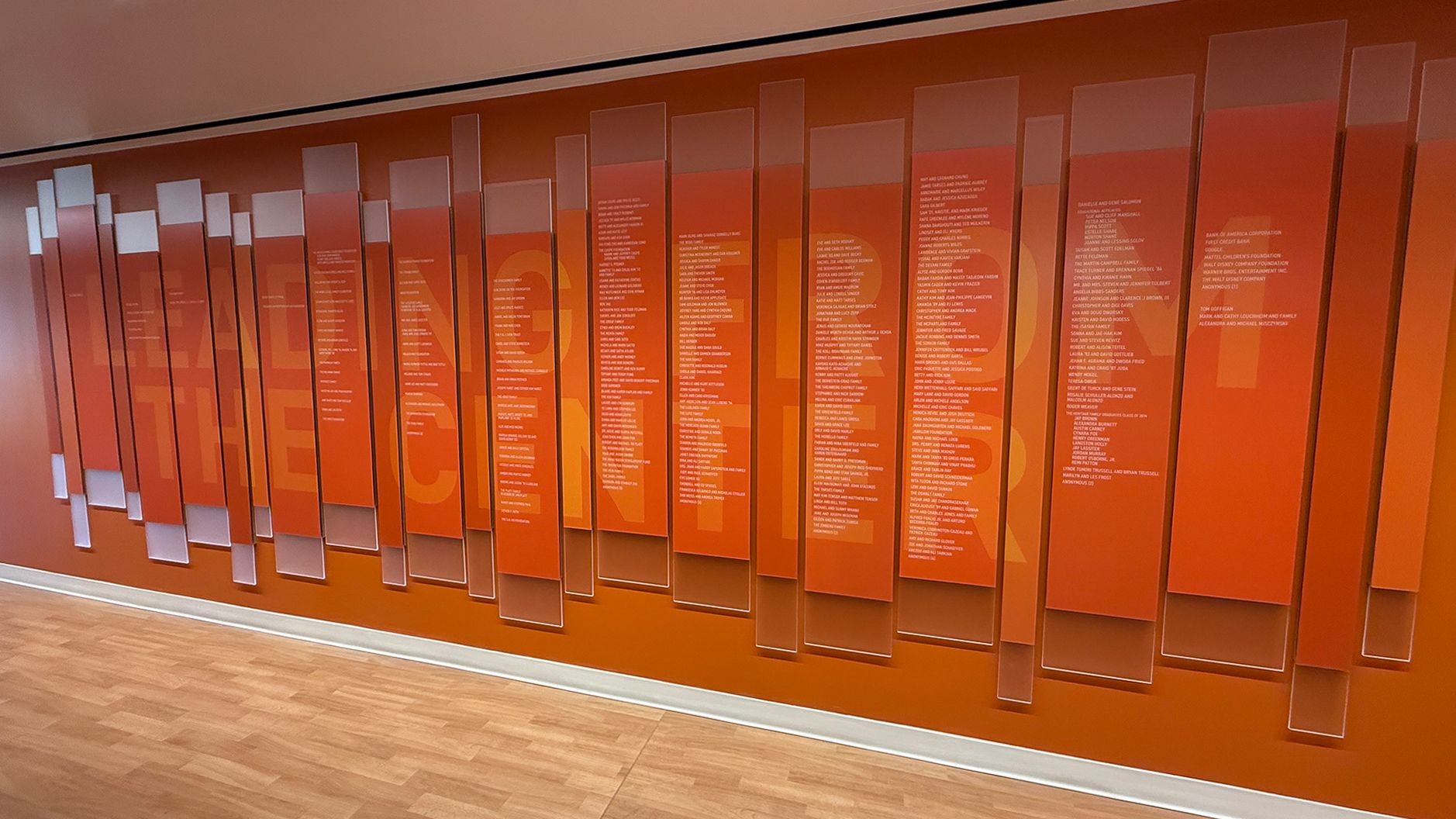 Modern education donor recognition wall with layered orange acrylic panels and donor names, creating a bold tribute to supporters in California.