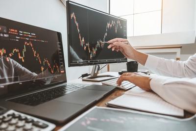 Trader testing a strategy on candlestick charts across laptop and monitor, representing Alpaca paper trading practice