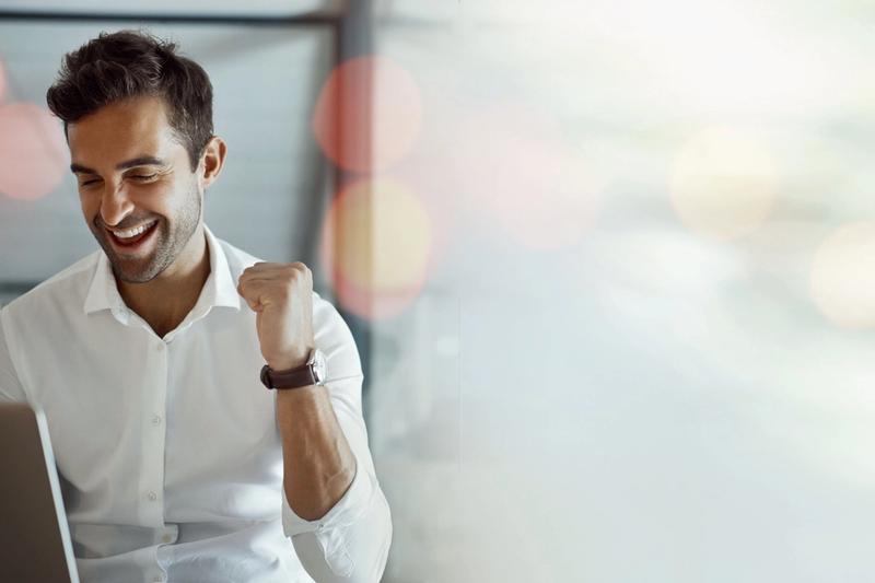 Smiling man in a white shirt making a fist pump while looking at a laptop in a bright office