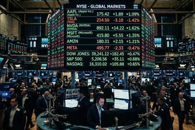 Busy NYSE trading floor with traders at monitors under a large ticker board of stock quotes and index prices