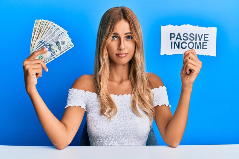 Woman holding a fan of US dollar bills and a paper sign reading Passive Income against a blue background
