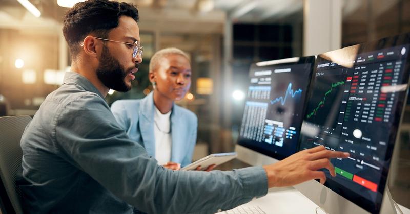 Financial advisor and investor reviewing automated portfolio dashboards on trading screens, representing Schwab automated investing options