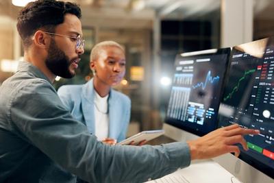 Financial advisor and investor reviewing automated portfolio dashboards on trading screens, representing Schwab automated investing options