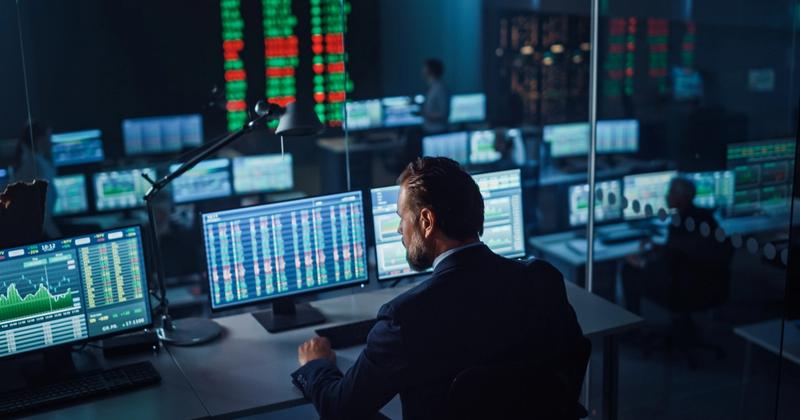 Trader reviewing multiple market data screens in a dark trading room, representing a hands-on Tradier brokerage review