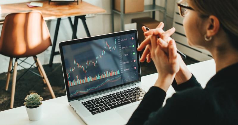 Woman at a desk with hands clasped, reviewing a long-term investment chart on a laptop for her Roth IRA