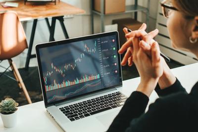Woman at a desk with hands clasped, reviewing a long-term investment chart on a laptop for her Roth IRA
