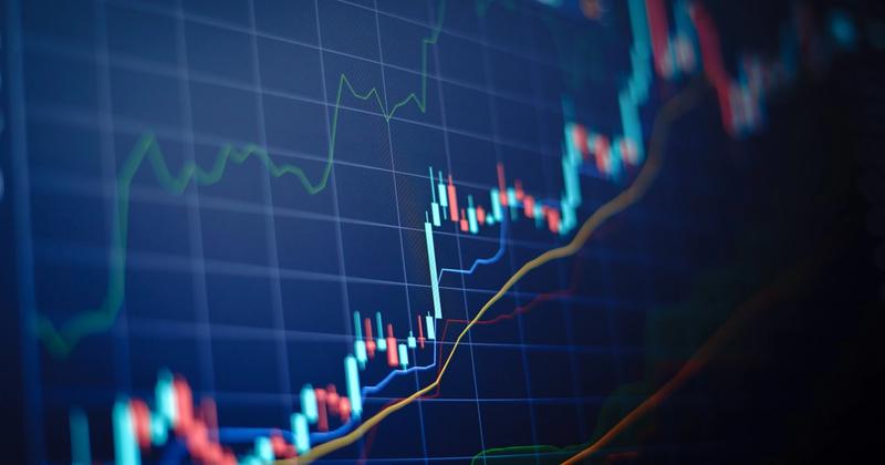 Close-up of a candlestick price chart on a dark blue screen with moving average and indicator lines
