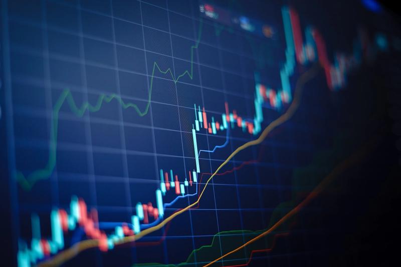 Close-up of a candlestick price chart on a dark blue screen with moving average and indicator lines