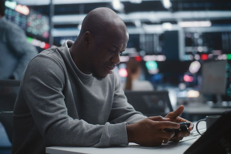 Trader at a desk checking an AI trading app on his phone, illustrating whether AI trading is legitimate