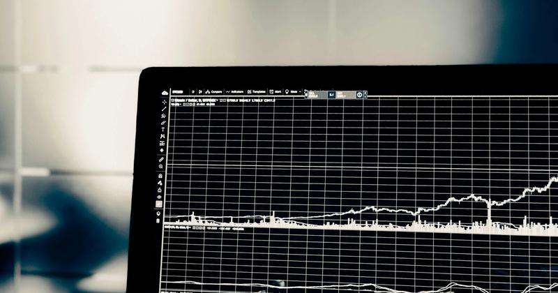 Black and white close-up of a screen showing a charting platform with a price line, volume bars, and indicator panels