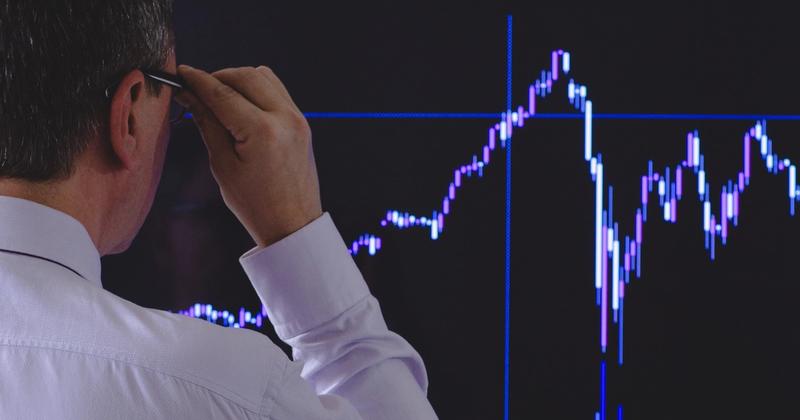 Analyst in a white shirt studying a sharply rising stock chart on a large screen, weighing whether AI stocks are in a bubble