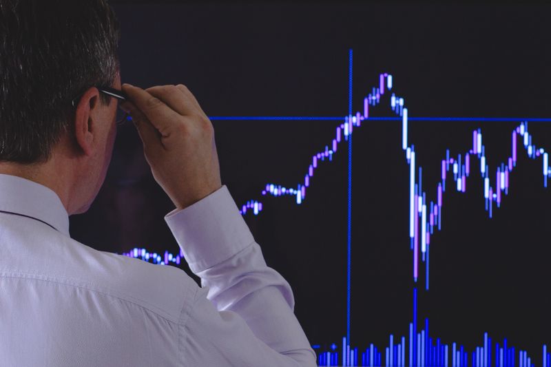 Analyst in a white shirt studying a sharply rising stock chart on a large screen, weighing whether AI stocks are in a bubble