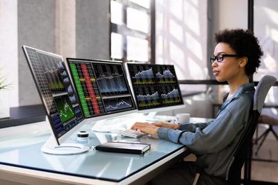 Trader at a multi-monitor desk running automated trading software connected to a brokerage API