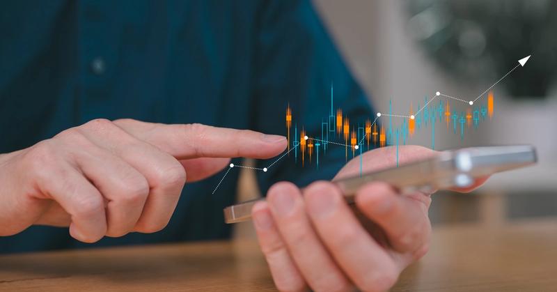 Hand holding a smartphone with rising candlestick chart projections, representing automated trading on the Webull mobile brokerage