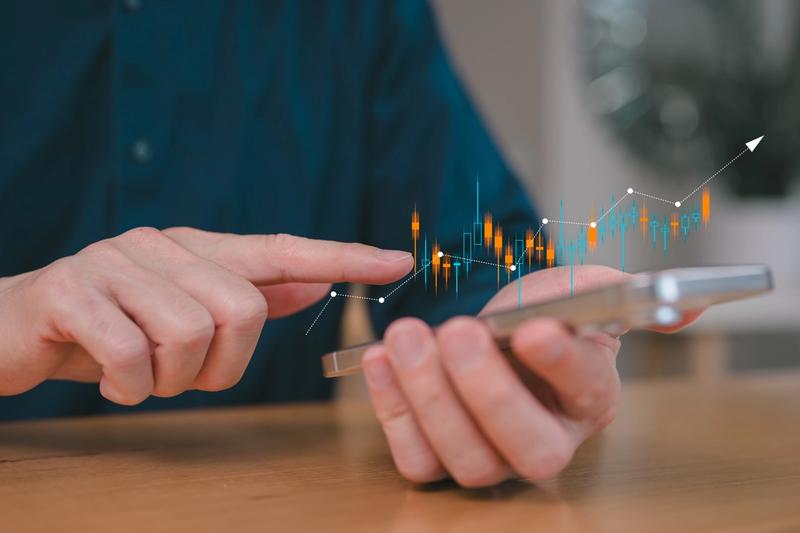 Hand holding a smartphone with rising candlestick chart projections, representing automated trading on the Webull mobile brokerage