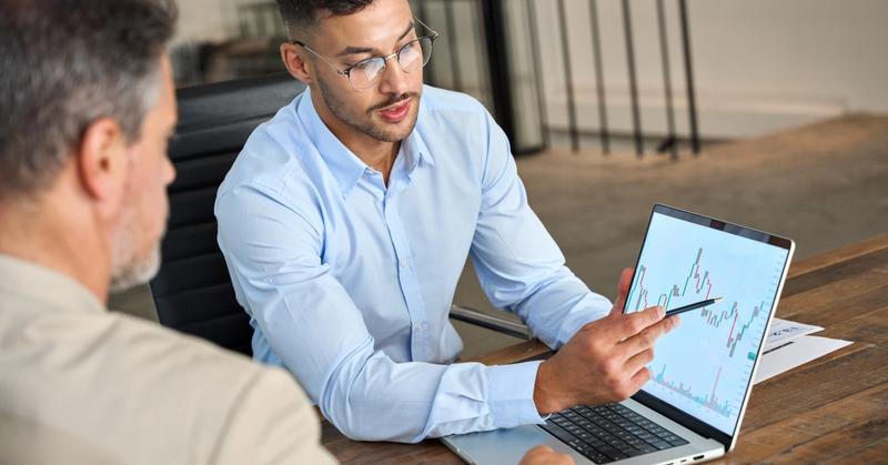 Two investors reviewing a stock chart together, illustrating one trader copying another trader's decisions