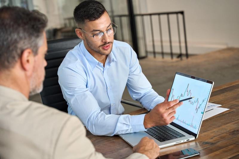 Two investors reviewing a stock chart together, illustrating one trader copying another trader's decisions
