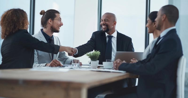 Business team at a conference table with a laptop and coffee cups as two colleagues shake hands
