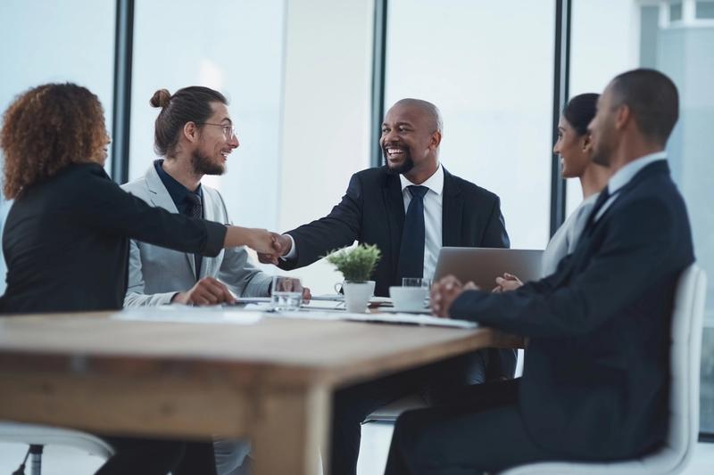 Business team at a conference table with a laptop and coffee cups as two colleagues shake hands