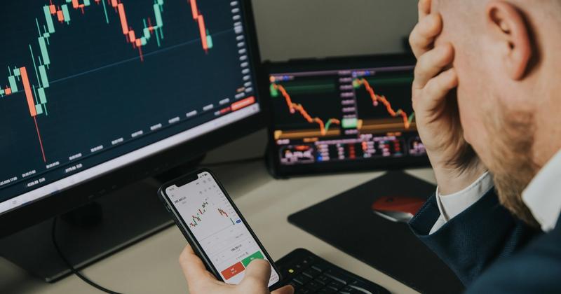 Trader at a multi-monitor desk reacting to falling stock charts after surprising economic news