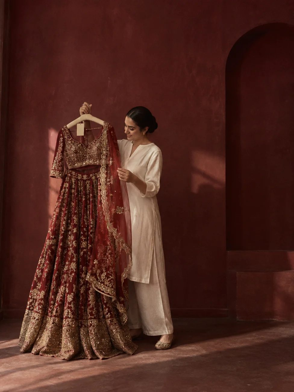 A woman holding up a red bridal lehenga on a hanger, with a price tag attached