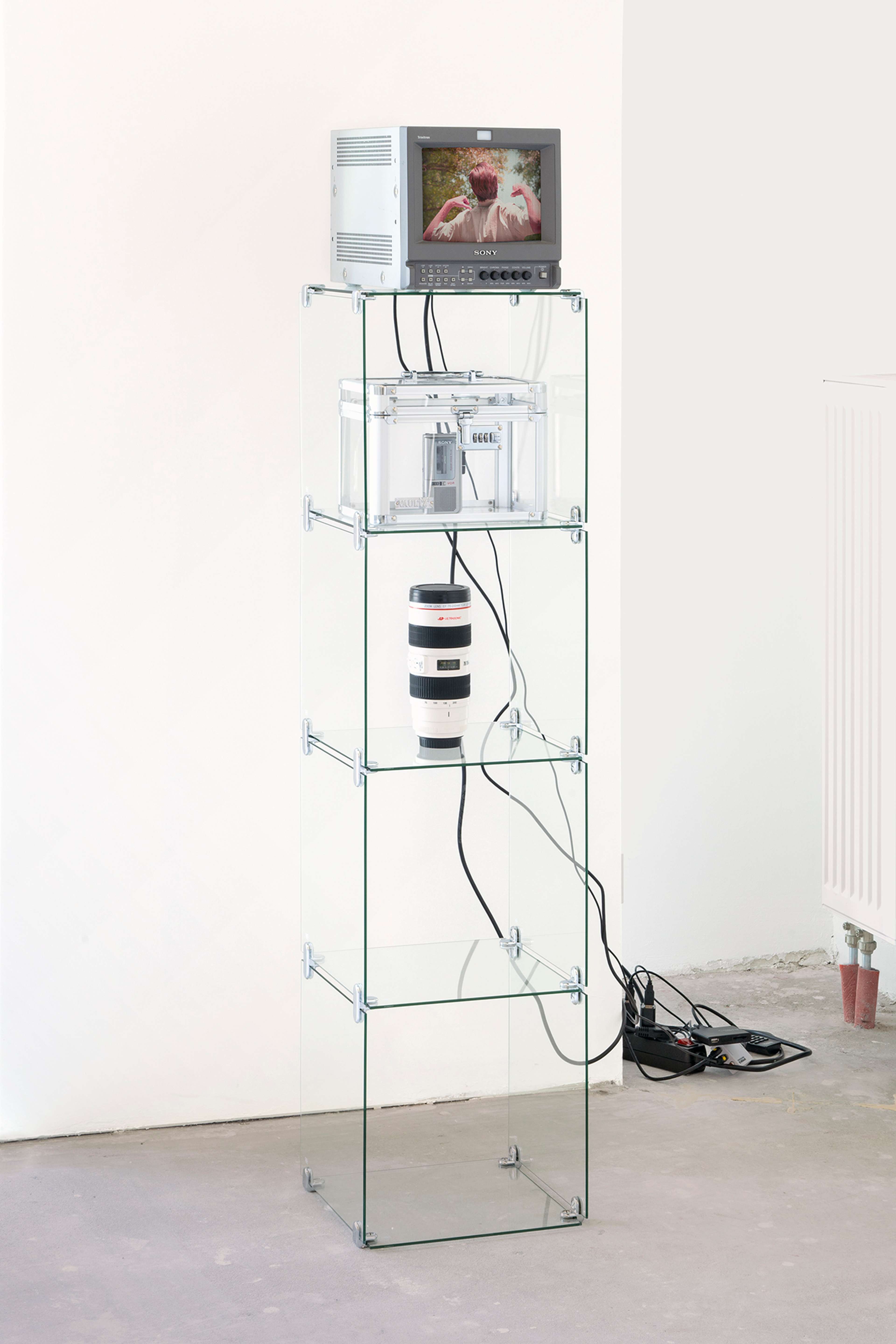 Kayode Ojo, I don’t want either of us to regret this, 2021, Sony Trinitron PVM-9L2 (2), Glass vitrine shelves (2), Vaultz Combination Lock Box Clear Acrylic and Steel (2), Sony Clear Voice Plus (2), Camera Lens Commuter Mug White (2), media player, video. Two parts, each: 61 3/4 x 12 5/8 x 15 3/4 in, 157 x 32 x 40 cm