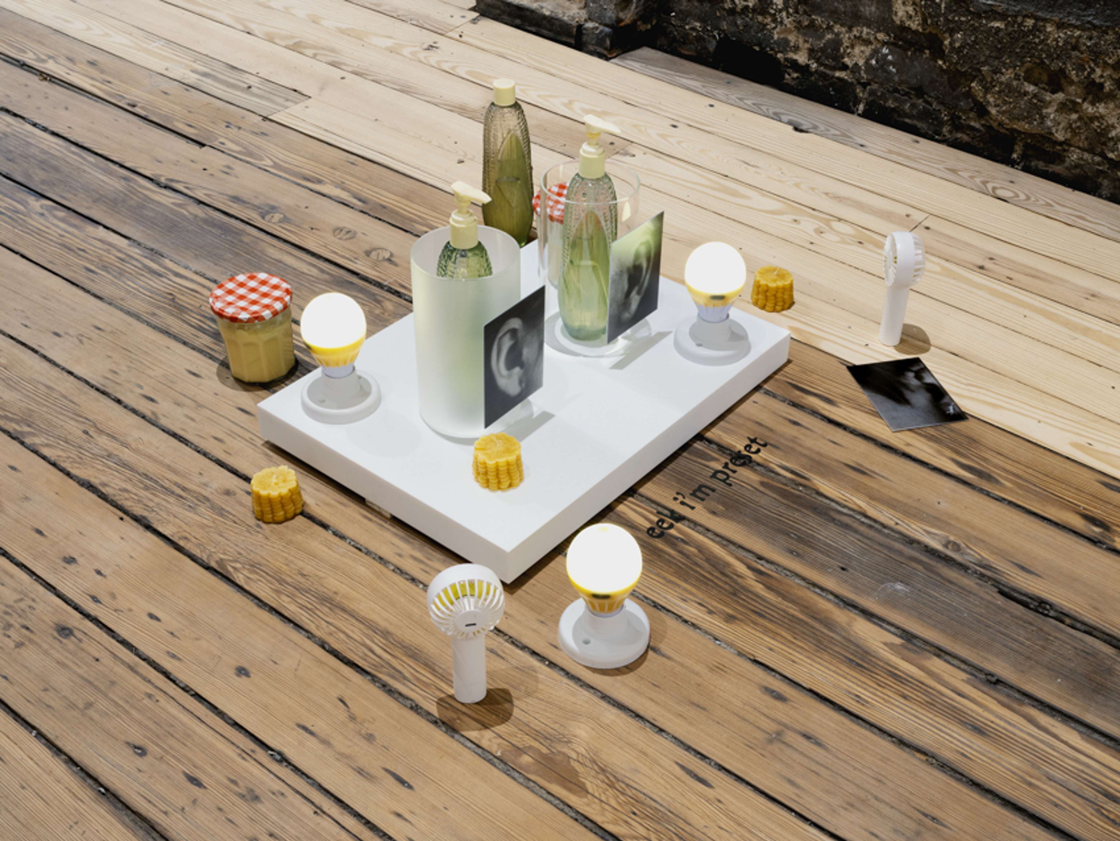 Jesse Stecklow, Cornspearacies (installation view) (2024). High fructose corn syrup; Avon Golden Harvest Hand Lotion bottles and lotion; beeswax candles; Lemonlights (beeswax, LED light bulbs, lamp bases, and hardware); jam jars; glass; UV print on acrylic; corian; springs; and fans; dimensions variable. Image courtesy of the artist and Dracula’s Revenge, New York and Sweetwater, Berlin. Photo: Jason Mandella.