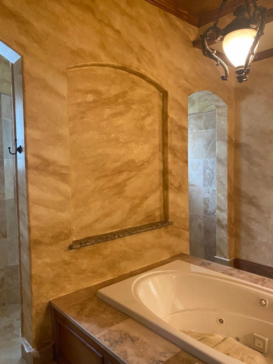 Burnished amber Venetian plaster in luxury master bathroom with arched niche above soaking tub and slate tile shower