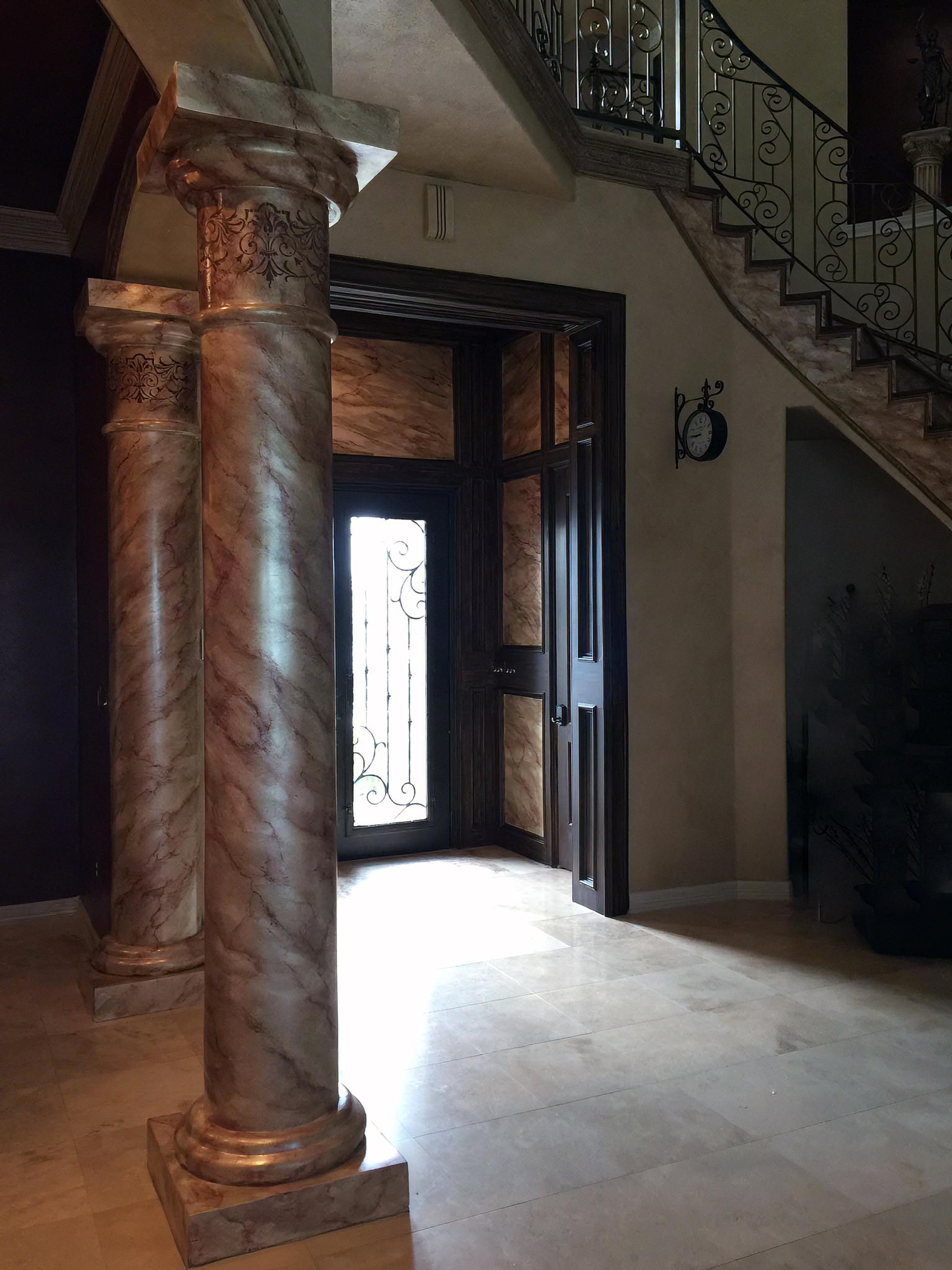 Faux marble columns with rose veining and gilded capitals in grand Houston foyer with matching marbleized entry door surround