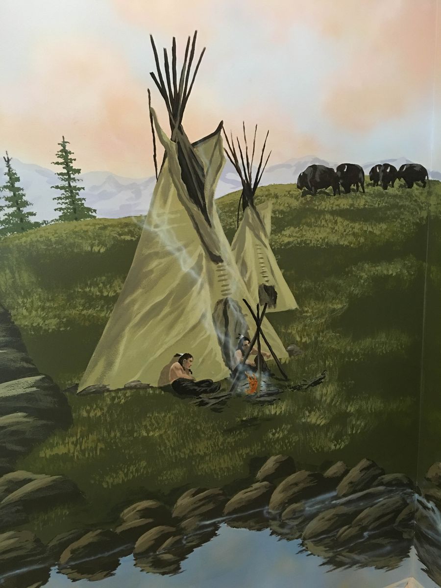 Hand-painted western frontier mural with teepees, campfire figures, bison herd, and rocky stream — immersive scenic wall art