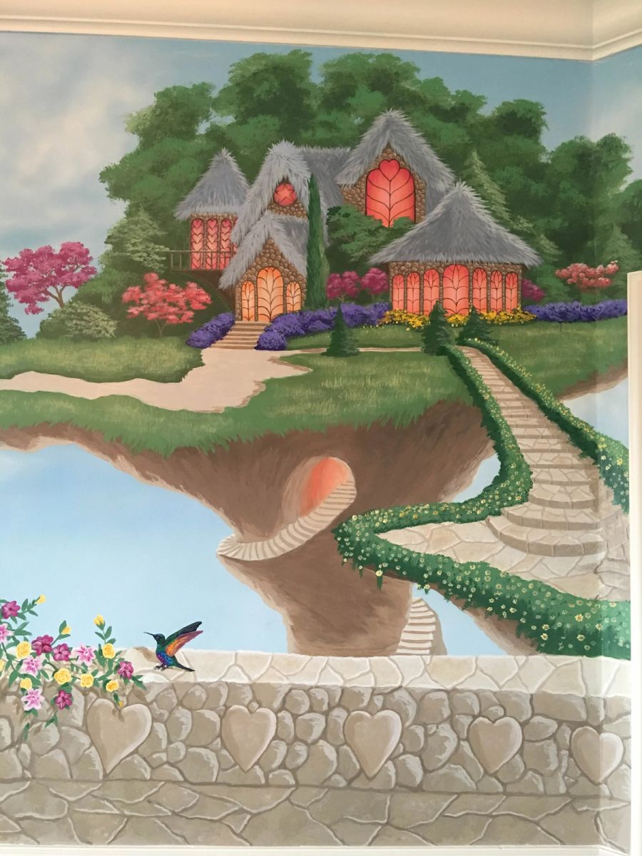 Hand-painted fantasy mural with floating island, thatched stone cottages, heart windows, and hummingbird on heart-stone wall.