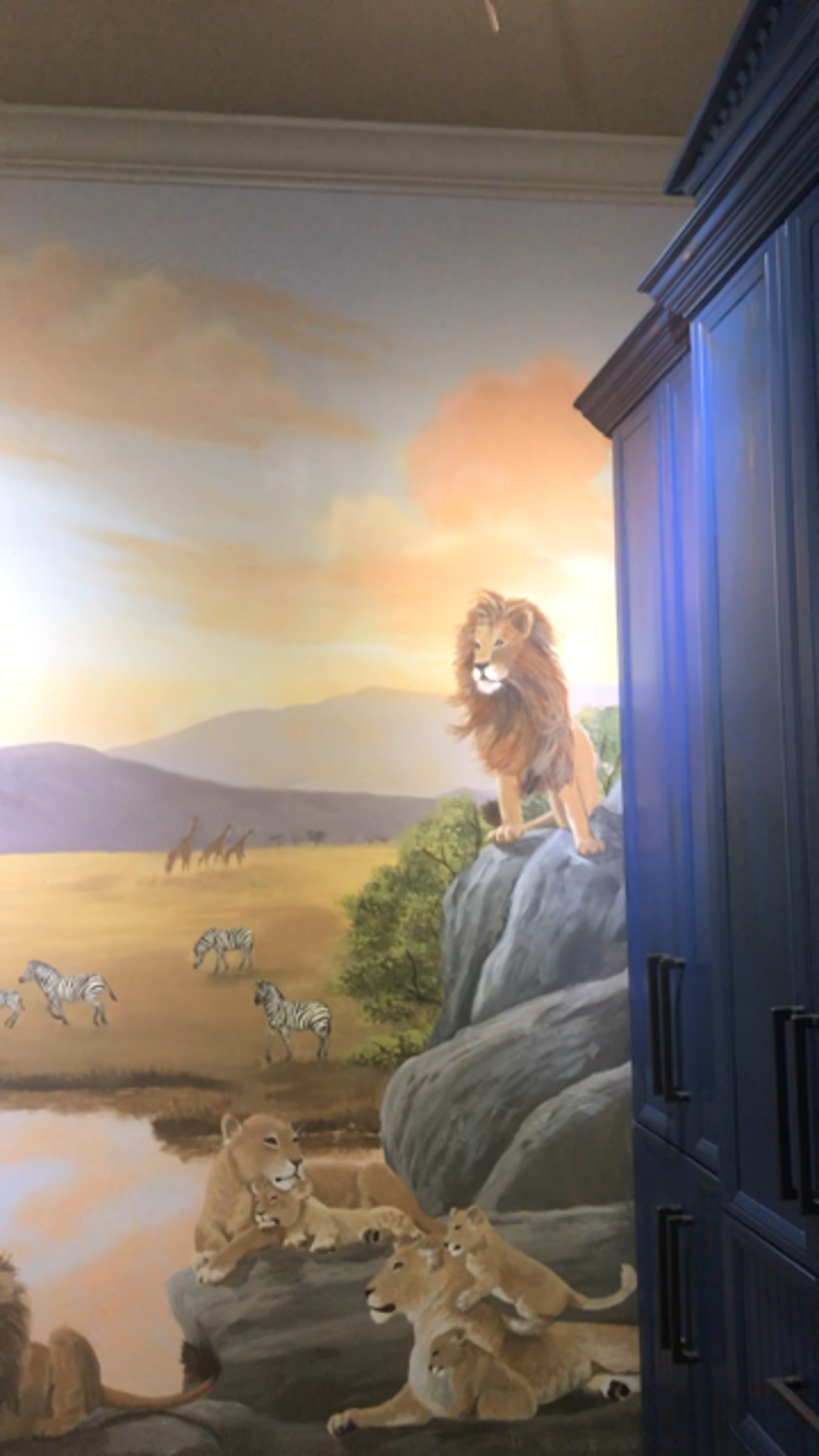 Hand-painted African savanna mural in children's bedroom with lion pride, zebras, and layered landscape depth.