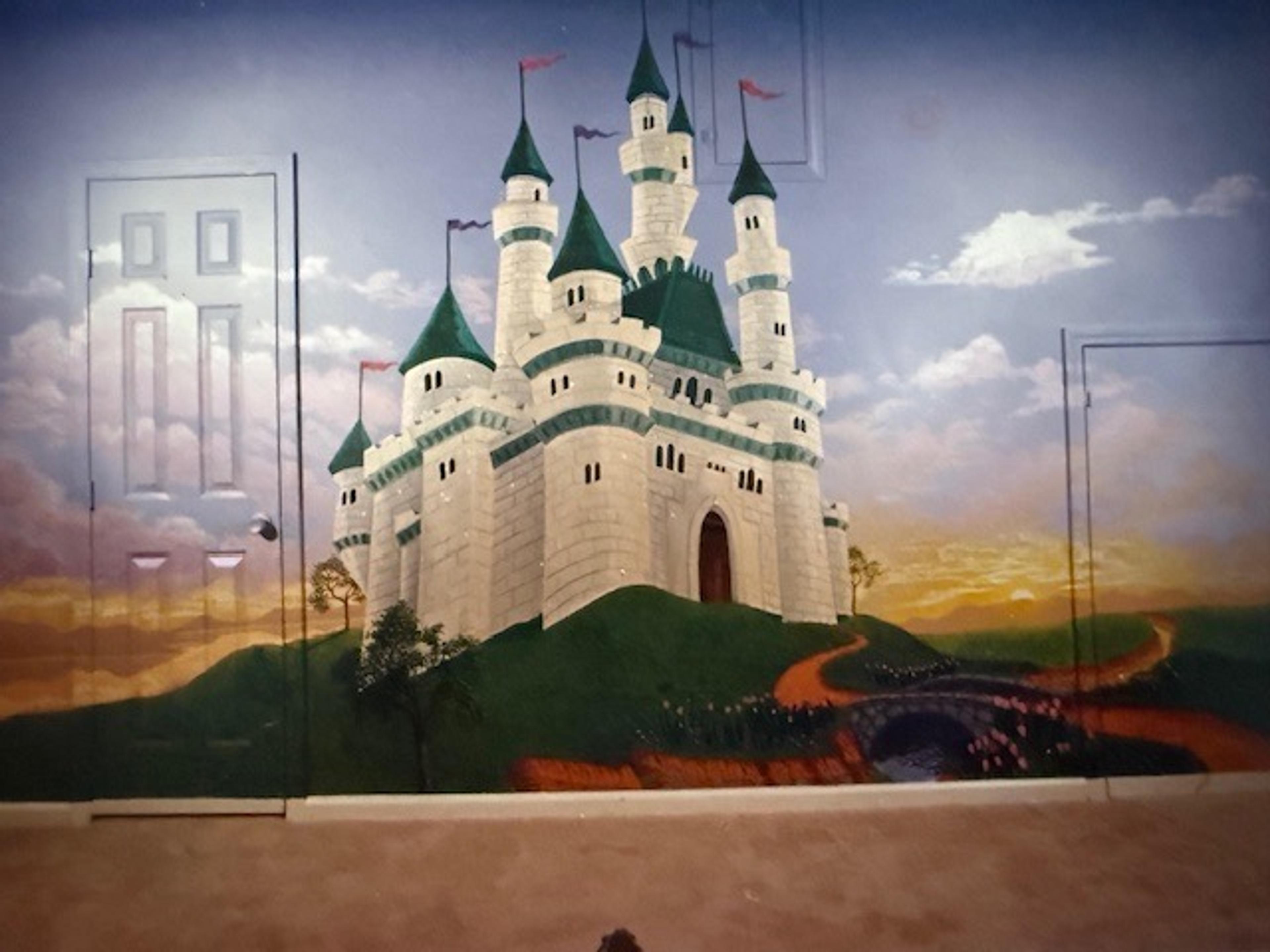 Hand-painted fairy tale castle mural in children's bedroom with green turrets, winding path, and trompe l'oeil door surrounds.