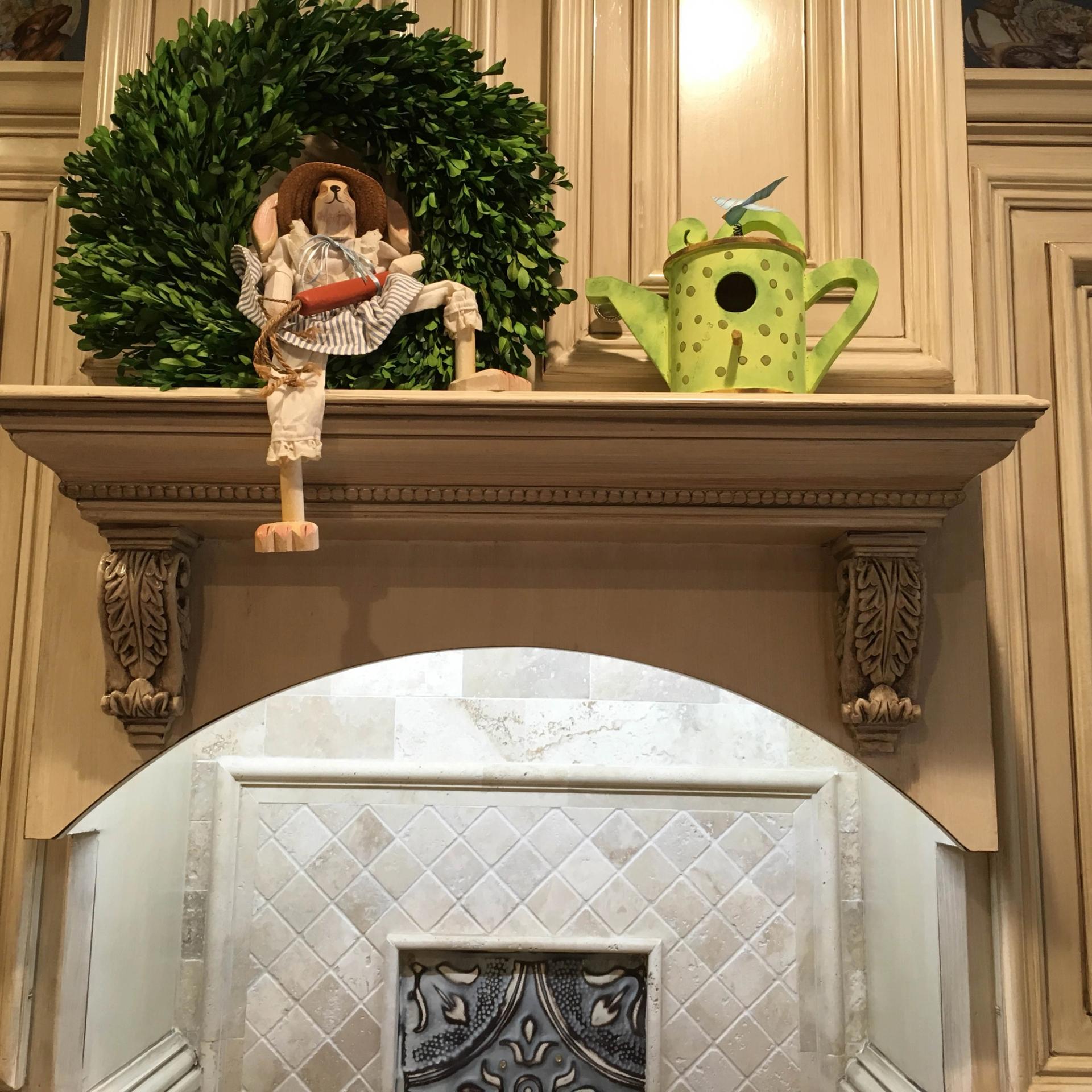 Antiqued glazed cream cabinetry with carved acanthus corbels framing arched travertine backsplash in luxury kitchen.