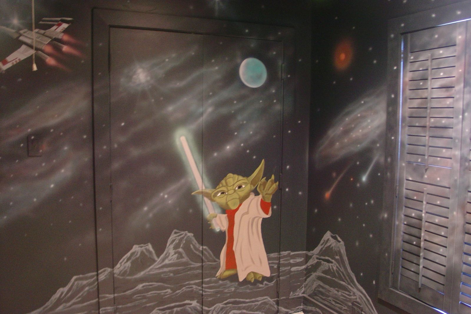 Hand-painted Star Wars children's bedroom mural featuring Yoda with lightsaber, space galaxies, and X-wing on dark walls