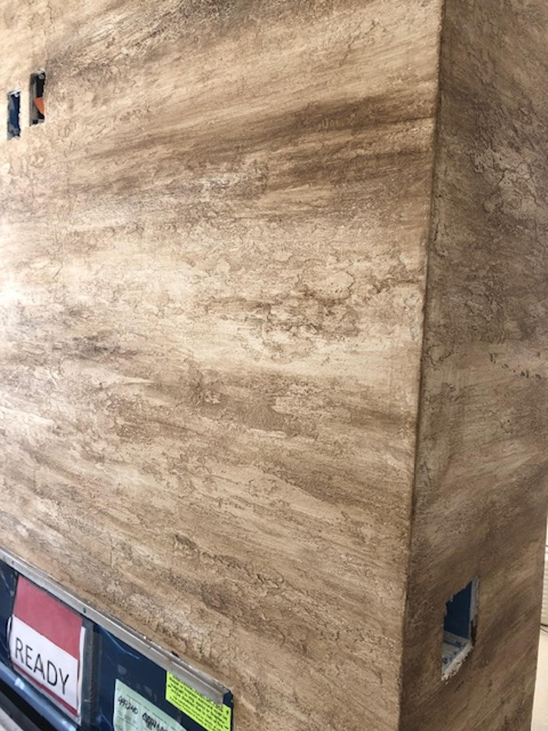 Faux travertine finish on architectural column with horizontal banding and pitting detail, residential interior, warm earth tones.