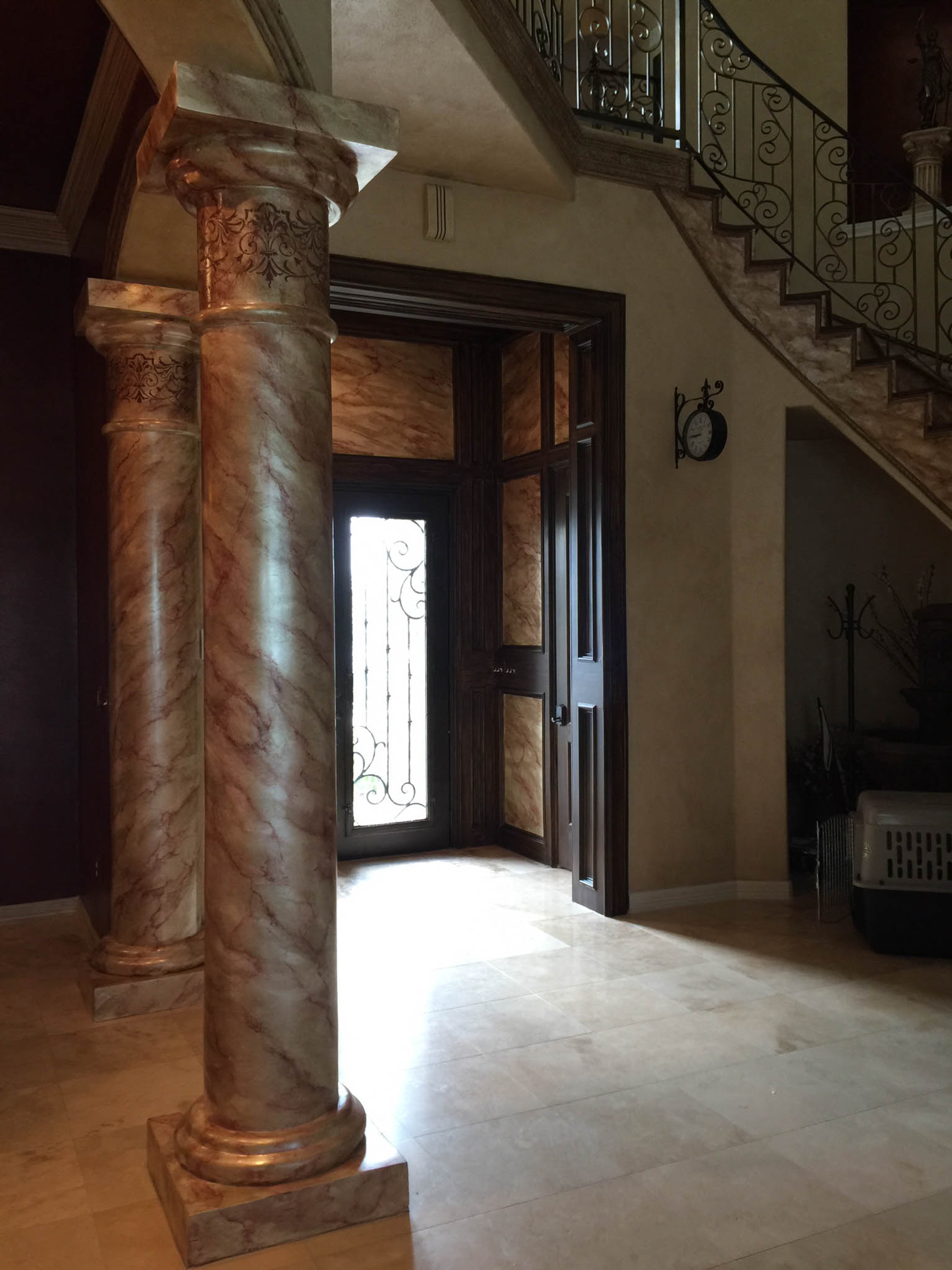 Faux marble columns with rose veining and gilded capitals in grand Houston foyer with matching marbleized entry door surround