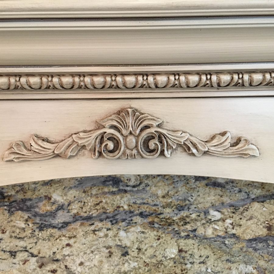 Antiqued cream glazed fireplace mantel with carved acanthus cartouche, egg-and-dart molding, and granite arch surround