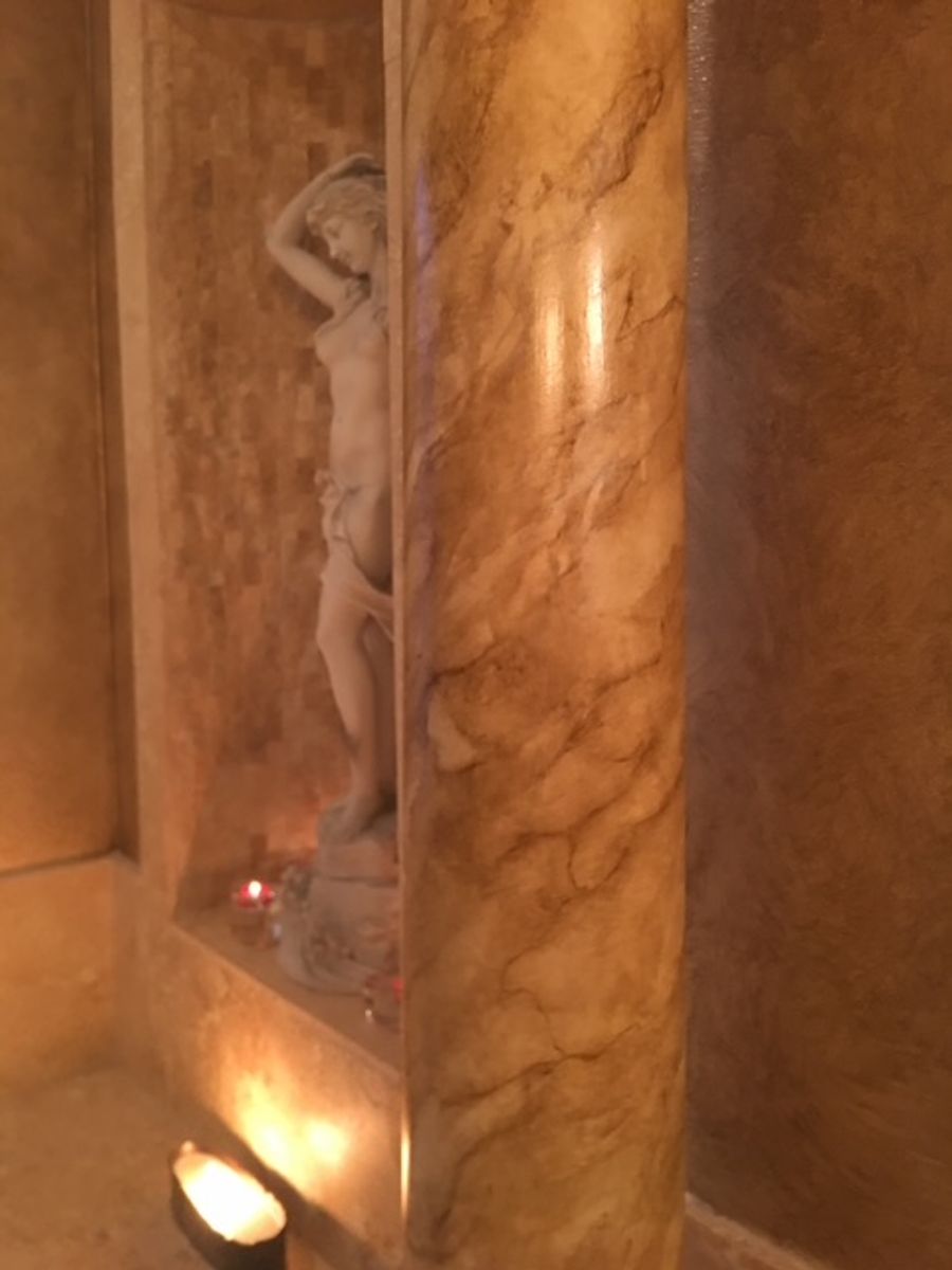 Honey onyx marbleizing in residential bathroom with amber veining on curved column and niche walls, candlelit setting.