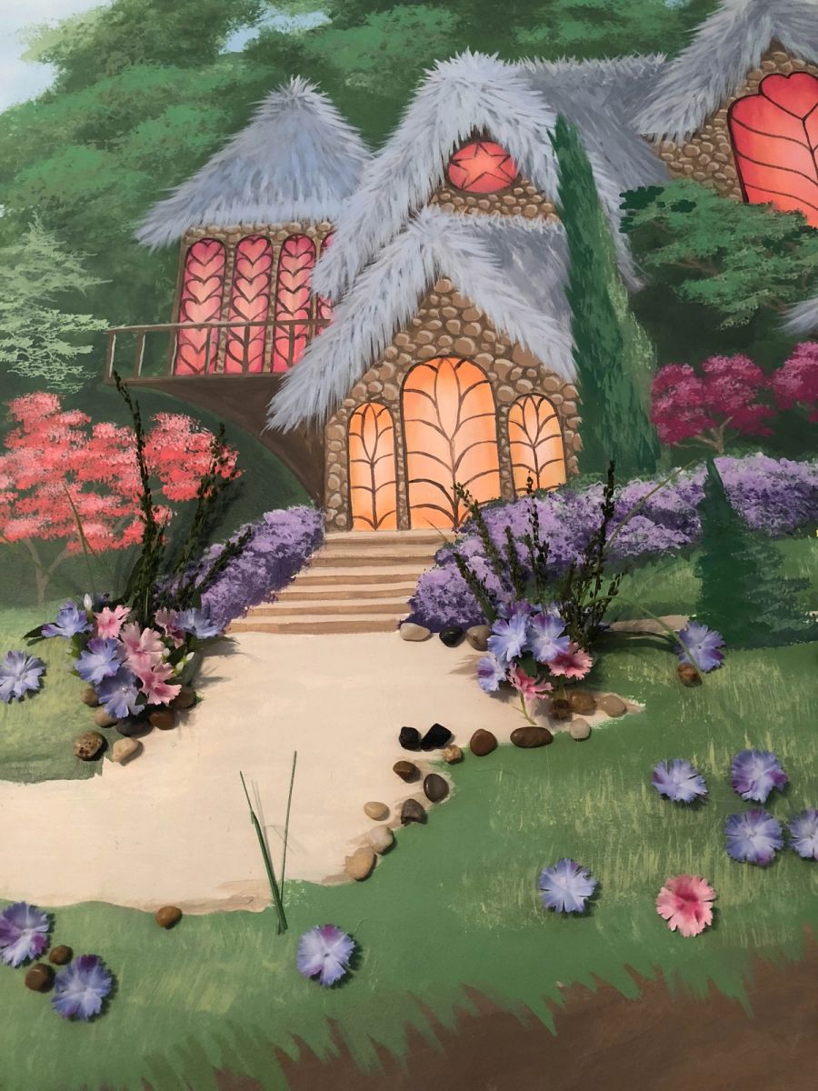 Hand-painted fairy-tale cottage mural with mixed-media flowers and stones for children's room, warm glowing windows.
