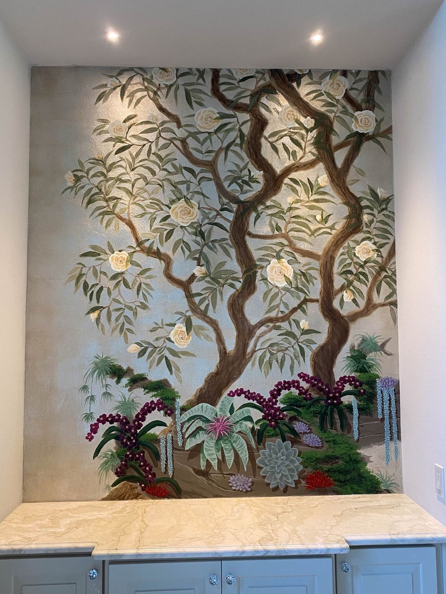 Chinoiserie hand-painted mural on metallic ground in kitchen niche above marble counter, featuring cream roses and tropical garden.
