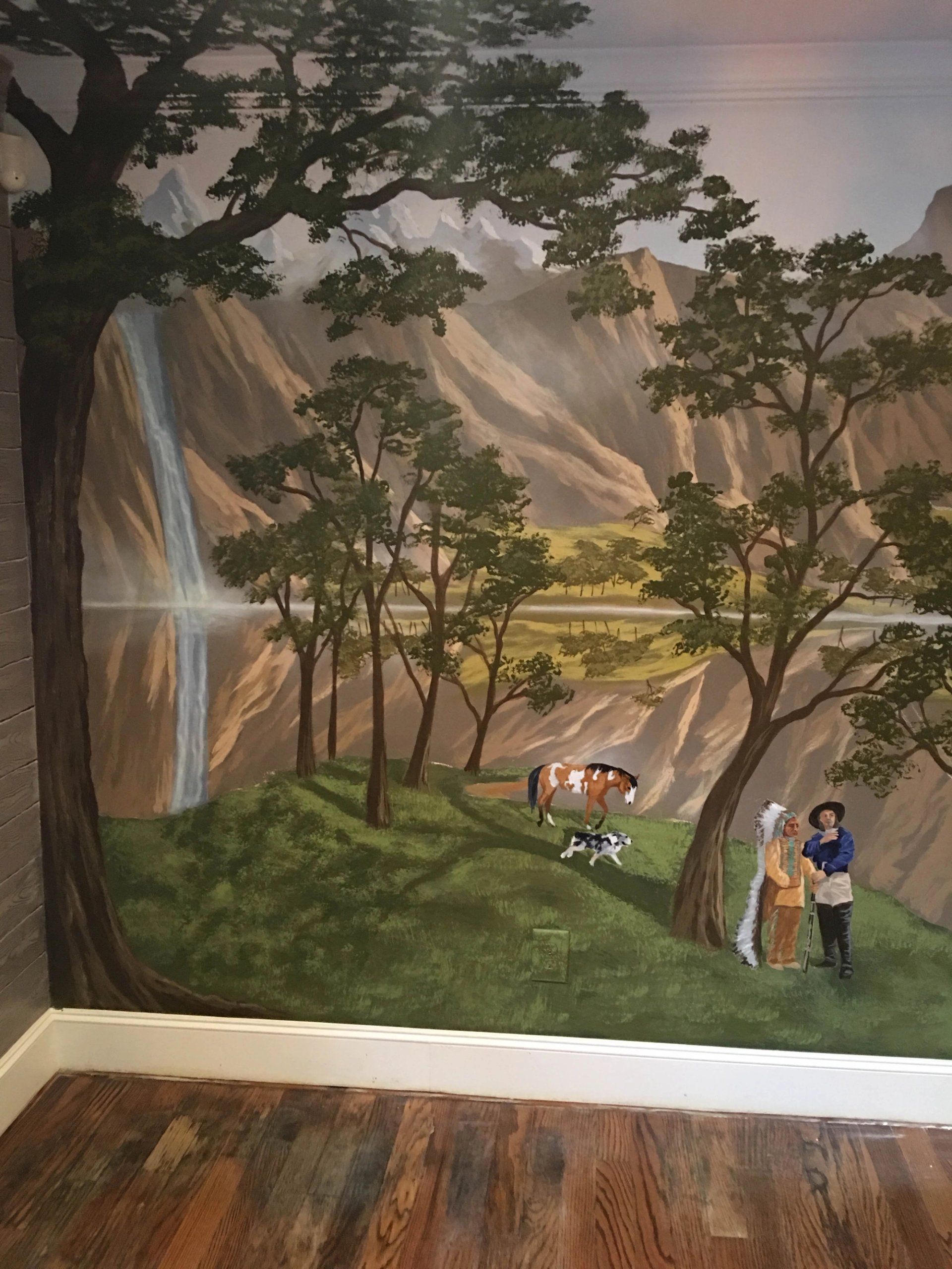 Hand-painted Western landscape mural with mountain waterfall, Native American and cowboy figures, and pinto horse on full wall.