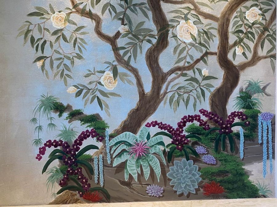 Hand-painted chinoiserie wall mural with cream roses, purple orchids, succulents, and cascading wisteria on blue sky background.