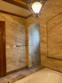 Aged travertine faux finish in warm amber tones covering full bathroom walls with arched tile niche and soaking tub, Houston TX