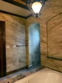 Aged travertine faux finish in warm amber tones covering full bathroom walls with arched tile niche and soaking tub, Houston TX