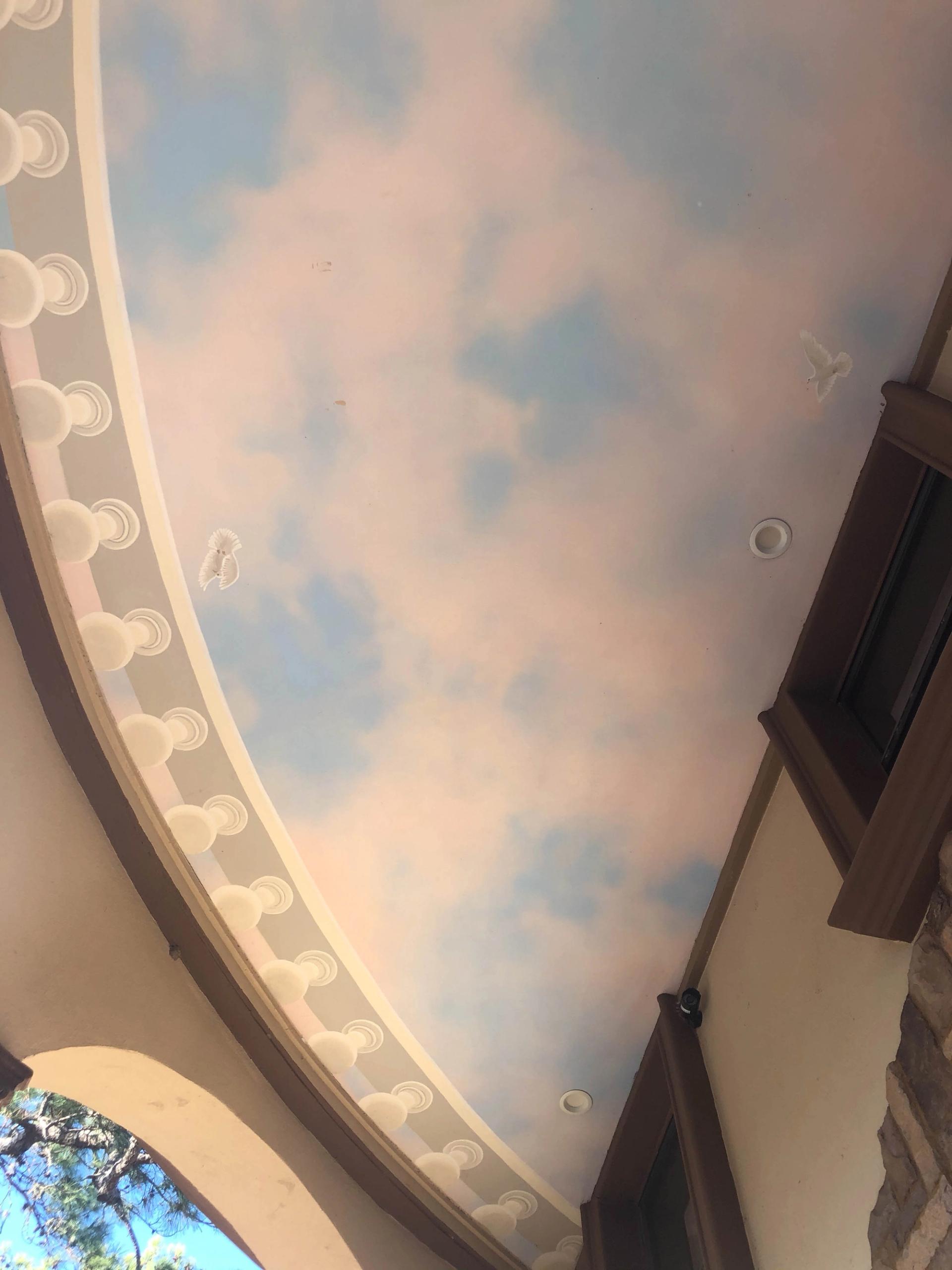 Hand-painted sky mural ceiling on curved outdoor loggia with trompe l'oeil balustrade border and white doves in flight.