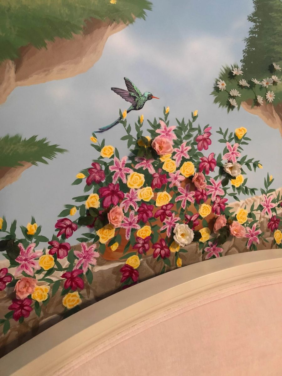 Hand-painted trompe l'oeil ceiling mural in children's bedroom with garden arch, hummingbird, and 3D floral appliqués