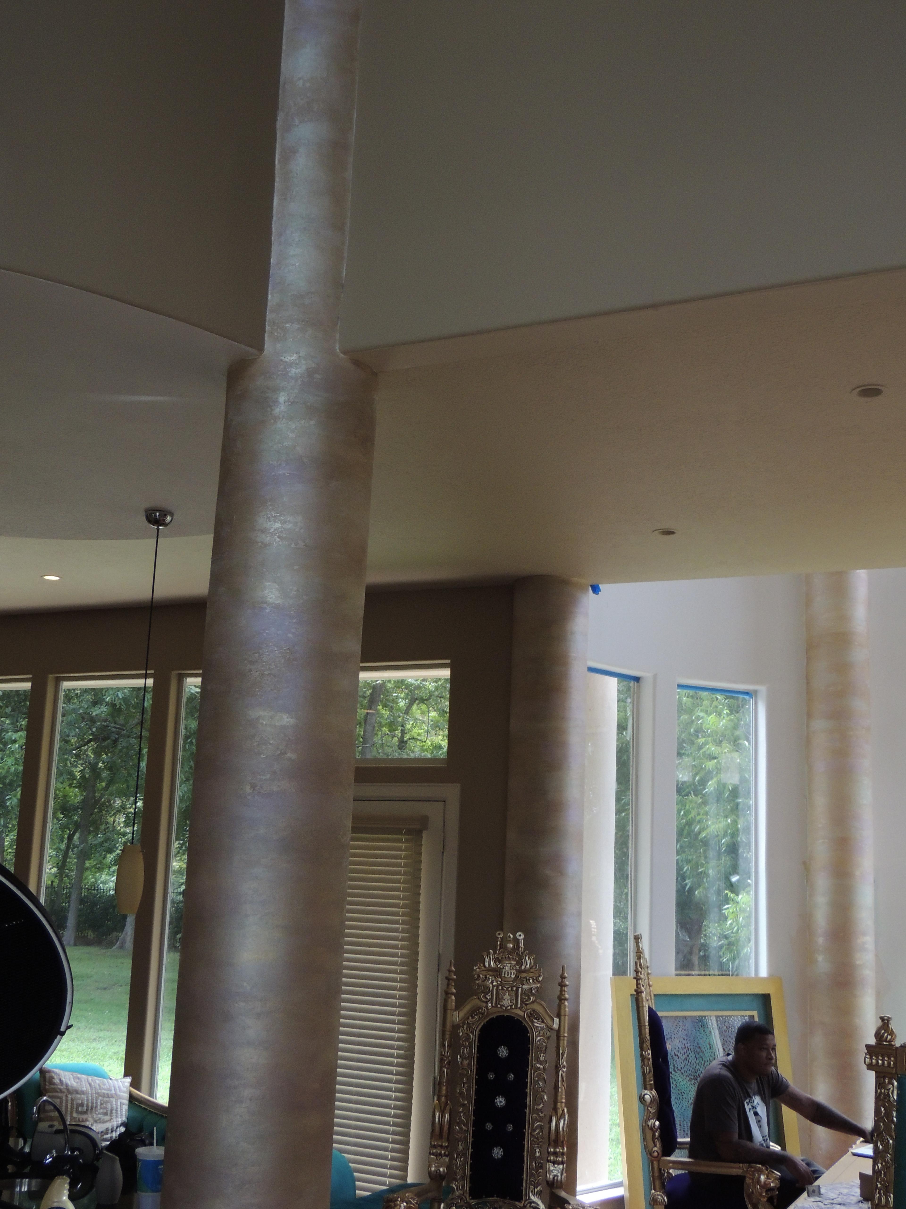 Travertine faux plaster finish on tall round columns in a grand residential great-room with warm taupe tones.