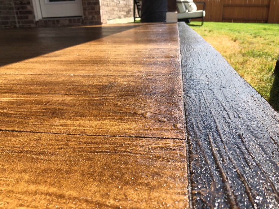 Faux-bois stamped concrete patio with amber acid stain and dark charcoal edge detail, Houston exterior finish.