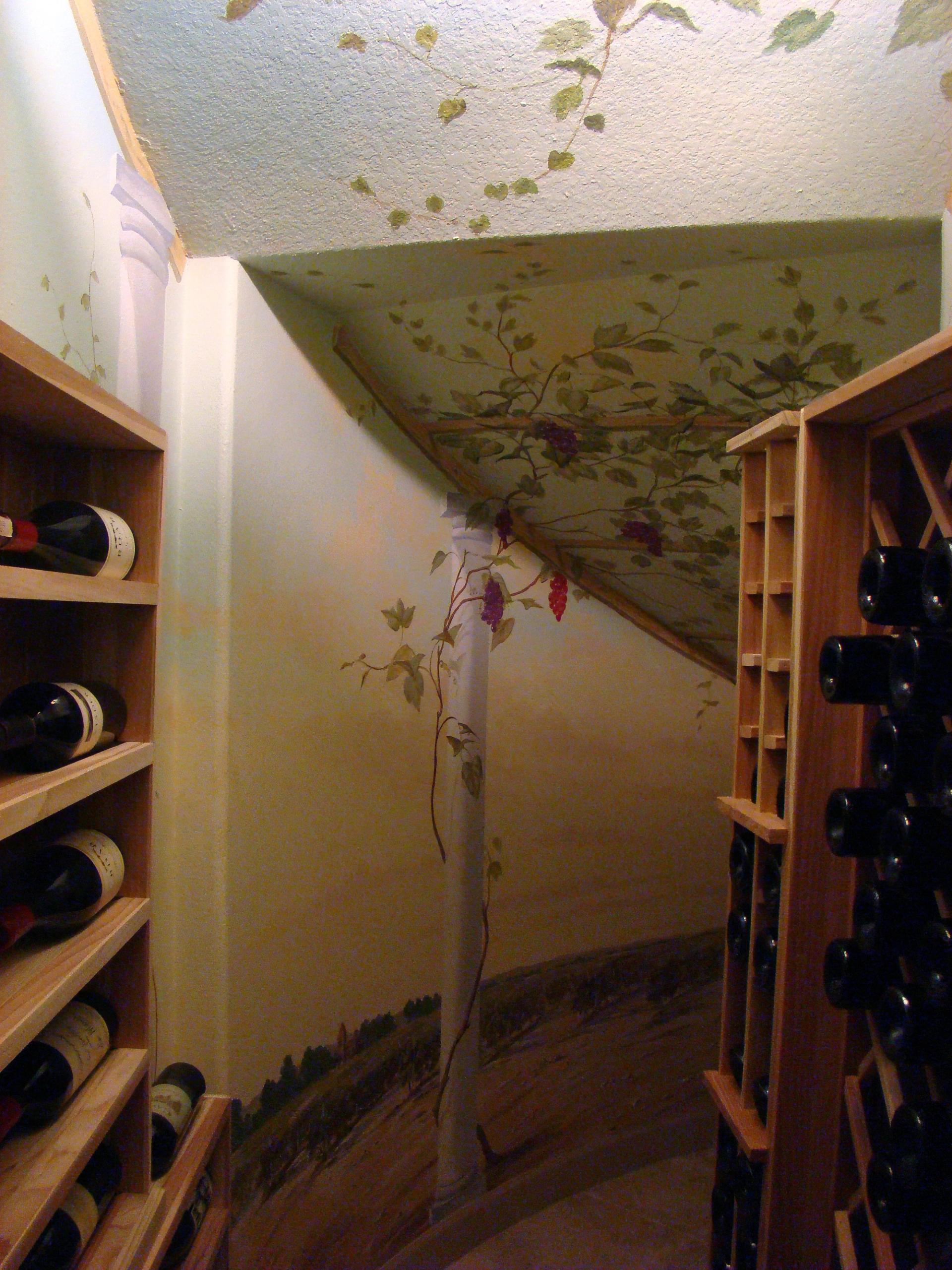 Hand-painted grapevine mural wrapping walls and angled ceiling of residential wine cellar with trompe l'oeil vineyard scene